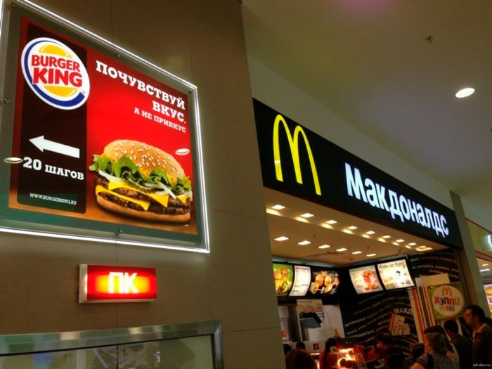 Рекламный плакат Burger King “Почувствуй вкус и не прирастёшь” рядом с вывеской ресторана Макдоналдс в торговом центре.